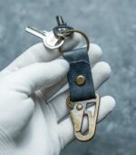 Detaliu carabină gold antichizat pe piele albastru navy, contrast hardware-piele vizibil, inel metalic secundar