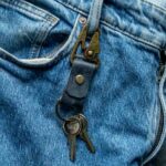 Detaliu breloc piele cu carabină navy prins la gaică blugi, carabină gold antichizat în prindere, piele naturală tăbăcită vegetal