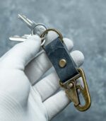 Breloc piele cu carabină albastru navy ținut în mână, dimensiuni 10x2,5 cm, ton închis sobru, tăbăcire vegetală