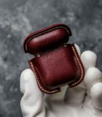 Husă AirPods 2 vișiniu, detaliu cusătură manuală bej saddle stitch, logo embossat, capsă silver, piele naturală