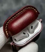 Husă AirPods 2 vișiniu vedere laterală, profil, cusătură bej saddle stitch, piele naturală, capsă silver, canturi vopsite