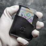 Portofel barbati pentru carduri, piele neagră mat, vedere frontală cu bancnotă introdusă în buzunar, logo embosat, cusătură neagră, handmade România